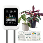 The Green Alcove 6-in-1 soil meter with its color screen lit, standing beside houseplants and the included plant care guide card